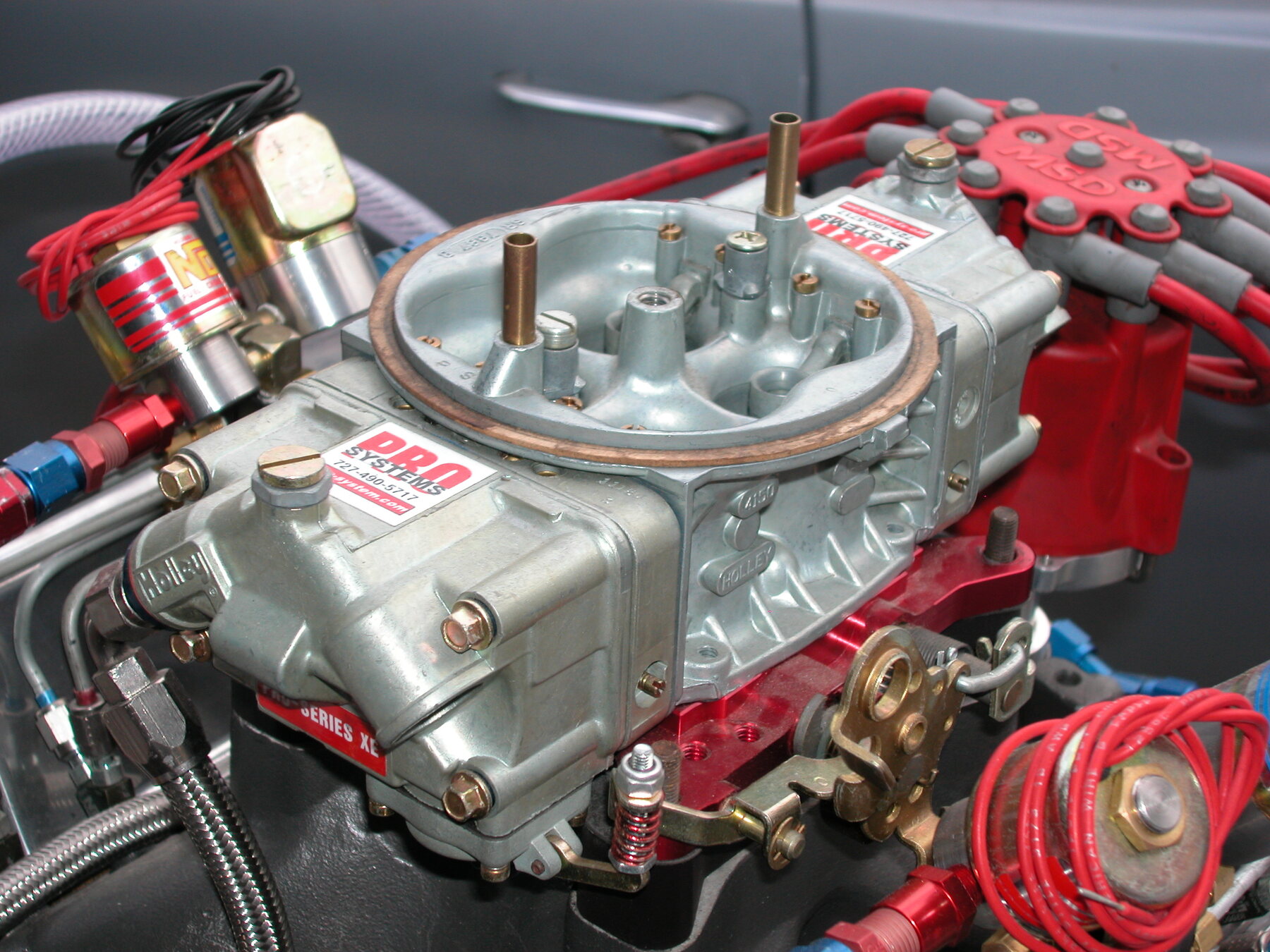 Un carburador de cuatro bocas de alto rendimiento sobre un V8, con sus cubas y conexiones a la vista.